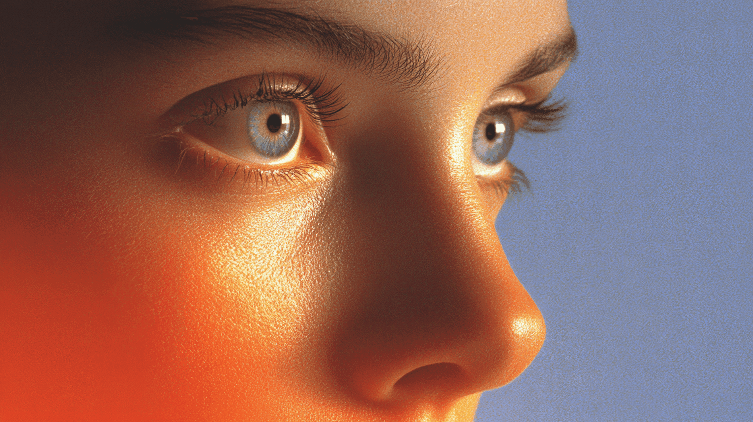Extreme close-up of blue eyes lit by warm orange light against a periwinkle background